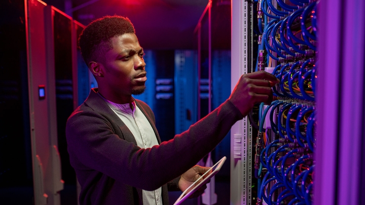 man concentrating on wire in server room holding tablet